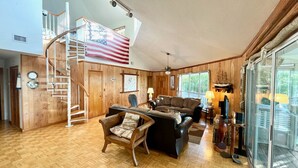 Un salón amplio con suelo de madera, una gran bandera estadounidense, una escalera y un portallamares de vidrio que da al exterior.