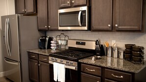 Una cocina moderna con electrodomésticos de acero inoxidable, armarios de madera oscura, encimeras de granito y una campana extractora de acero inoxidable.