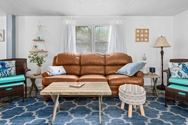 A living room with a brown leather sofa, a wooden coffee table, and blue patterned rugs.