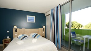 A hotel room with a bed, two bedside lamps, a nightstand, a window with curtains, and a view of the outdoors.