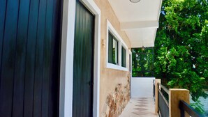 A covered outdoor corridor with a stone wall, a wooden door, and a metal railing. - Habitaciones Colonial Zaci (Valladolid)