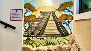 A mural of a pyramid with a sunset, a sign inviting visitors to the rooftop on the third floor, and a stone wall. - Habitaciones Colonial Zaci (Valladolid)