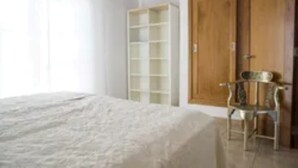 Un dormitorio con una cama, un armario de madera, una silla y una estantería blanca.