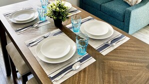 Een eetgedeelte met een houten tafel voor vier personen, blauwe glazen en een potplant.