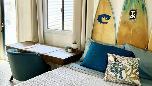 Een slaapkamer met een bed, een bureau en twee surfplanken tegen de muur.