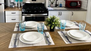 Een moderne keuken met een witte betegelde spatwand, roestvrijstalen apparatuur en een houten eettafel voor vier personen.