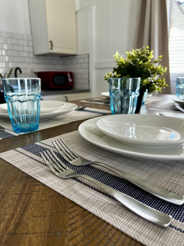 A dining table set with plates, glasses, and cutlery, with a microwave and potted plant in the background.