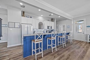 A modern kitchen with white cabinets, a blue island, and wooden bar stools. - Boat Dock Access: Waterfront Freeport Home! (Freeport)