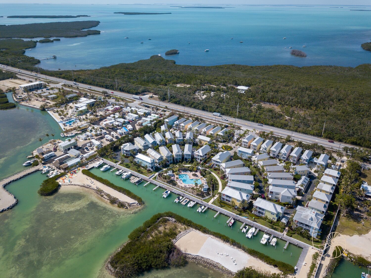 Vista aérea de un complejo turístico costero con varias edificaciones, un puerto deportivo y una piscina.