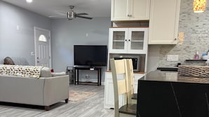 A modern living room with a sofa, TV, and dining area with cabinets and a microwave.