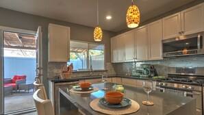 A modern kitchen with white cabinets, a central island with a glass top, and pendant lighting.