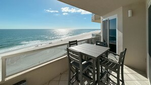 A balcony with a table and chairs overlooking a beach. - Enclave 803 - is a Family Friendly Beach Front condo! (Orange Beach)