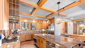 Una cocina amplia con gabinetes de madera, una isla grande, electrodomésticos de acero inoxidable y vistas al bosque a través de amplios ventanales.