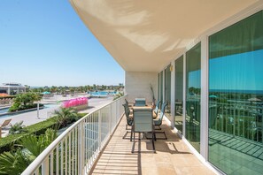 Ein Balkon mit Blick auf einen Pool und den Resortbereich, inklusive Liegestühlen und einer Glasreling.