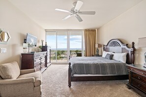 Ein Schlafzimmer mit einem Bett, einem Sessel, einer Kommode, einem Deckenventilator und einem großen Fenster mit Blick.