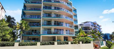 A multi-story hotel with balconies, a swimming pool, and a well-maintained garden.