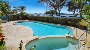 A swimming pool with a curved edge, surrounded by a stone deck and lush greenery. - PICNIC7- PICTURE PERFECT PICNIC POINT (Maroochydore)