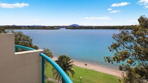 A view of a lake with a beach, a mountain in the background, and a building with a balcony overlooking the water. - PICNIC7- PICTURE PERFECT PICNIC POINT (Maroochydore)