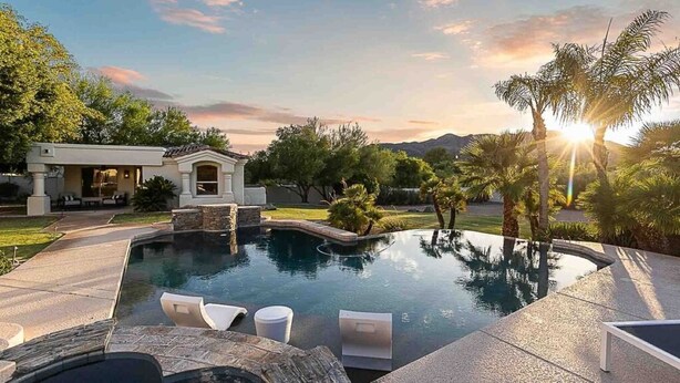 Piscina con sillas de descanso, un porche cubierto y vistas a montañas.