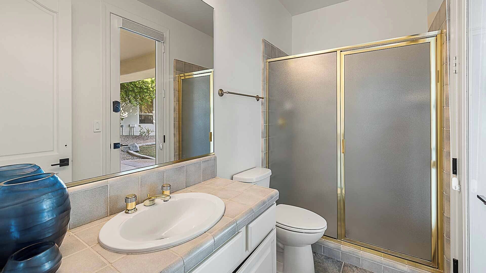 Un baño con un espejo grande, un lavabo, un inodoro y una cabina de ducha con vidrio esmerilado.