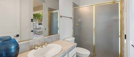 Un baño con un espejo grande, un lavabo, un inodoro y una cabina de ducha con vidrio esmerilado.