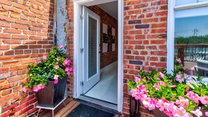 A brick building with a white door leading to an interior space. There are potted plants with pink flowers on the ground and a small table with a chair outside. - artsy downtown river view condo (Wilmington)
