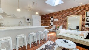 A modern kitchen with white cabinetry, a central island, and bar stools. - artsy downtown river view condo (Wilmington)