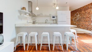 A modern kitchen with a central island, white bar stools, and a brick accent wall. - artsy downtown river view condo (Wilmington)