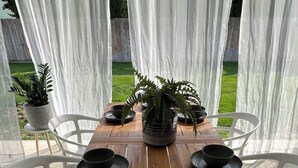 A wooden table set with black bowls and plates, surrounded by white chairs, in a covered outdoor area with a view of a grassy yard. - Enjoy a stylish experience at The Franklin (Pasco)