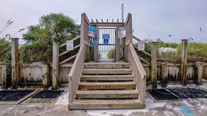 A wooden staircase leading to a gated entrance with multiple signs, including a 'Beach Access' sign. - 2BR/2BA Beach front Sleep8 Balcony-Gated Community (Panama City Beach)