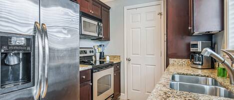 A kitchen with stainless steel appliances, a granite countertop, and dark wooden cabinets.