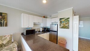 A compact kitchen with white cabinets, a stainless steel refrigerator, and a microwave. - Gone to the Beach Gulf Front Studio Pet Friendly (Navarre Beach)