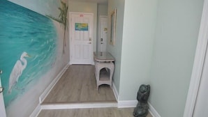 A hallway with a mural of a beach scene, a white door, a small white stool, and a statue. - Gone to the Beach Gulf Front Studio Pet Friendly (Navarre Beach)