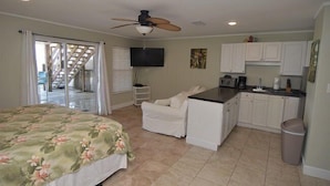 A bedroom with a bed, a white chair, a kitchenette, and a ceiling fan. - Gone to the Beach Gulf Front Studio Pet Friendly (Navarre Beach)