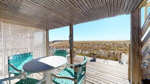 A covered outdoor area with a table and chairs, a wooden deck, and a view of a beach and dunes. - Gone to the Beach Gulf Front Studio Pet Friendly (Navarre Beach)