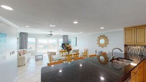 A modern kitchen with a central island, dining area with chairs, and a view of the outdoors. - Island Time Gulf-Front Townhome/ Pet Friendly (Navarre Beach)