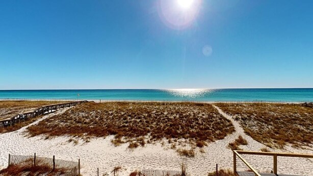 A beach with a wooden boardwalk leading to the water, sandy dunes, and a clear blue sky. - Island Time Gulf-Front Townhome/ Pet Friendly (Navarre Beach)