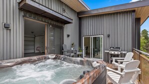 A hot tub on a wooden deck with outdoor furniture and a grill.