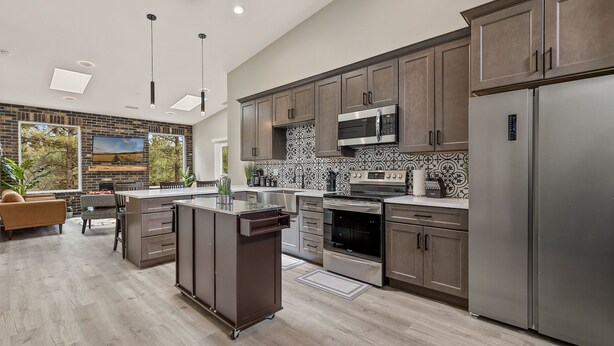 A modern kitchen with stainless steel appliances, a central island, and a large window overlooking greenery.