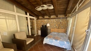 A bedroom with a bed, a sofa, a dresser, and a stone wall. - cozy guest house  (Navas del Rey)