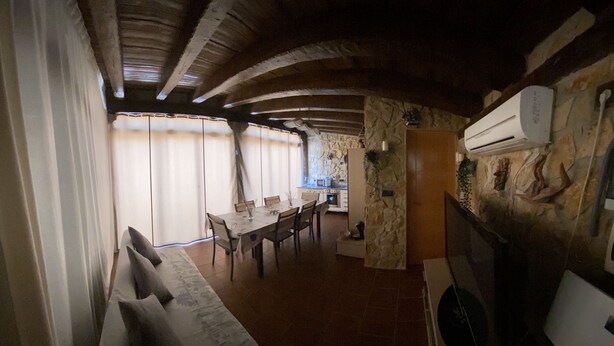 A dining area with a table and chairs, a stone wall with a mounted air conditioner, and a window with curtains. - cozy guest house  (Navas del Rey)