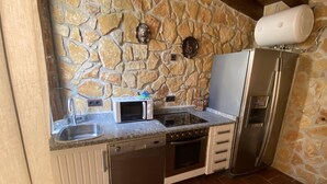 A kitchen with a stone wall, a microwave, a stove, a sink, and a refrigerator. - cozy guest house  (Navas del Rey)