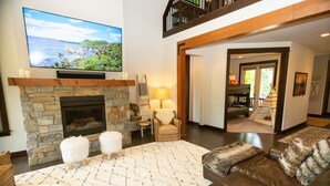A living room with a stone fireplace, a large flat-screen TV, a sofa, and a patterned rug. - FAll in Suncadia! Walk to the new Suncadia social & Golf! Hot Tub and Games! (Cle Elum)