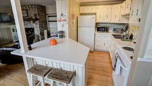 Una cocina con armarios blancos, una isla blanca con taburetes, una chimenea de piedra y un microondas.