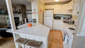 A kitchen with white cabinets, a white island with stools, a stone fireplace, and a microwave.