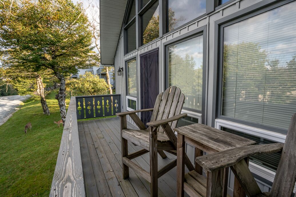 A wooden deck with a chair and table, a glass door, and a view of a tree and grass.