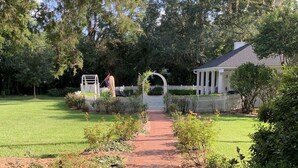 Ein gepflegter Garten mit Rasen und Bäumen, durch den ein Ziegelweg zu einem weißen Gartenpavillon führt.