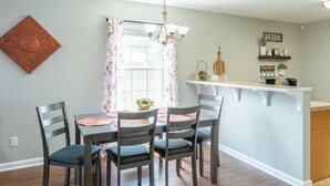 A dining area with a table and chairs, a chandelier, a window with curtains, and a kitchen counter with shelves. - Clean+Cozy+Close to Airport/Jackson/Dogwood Ctr! (Brandon)