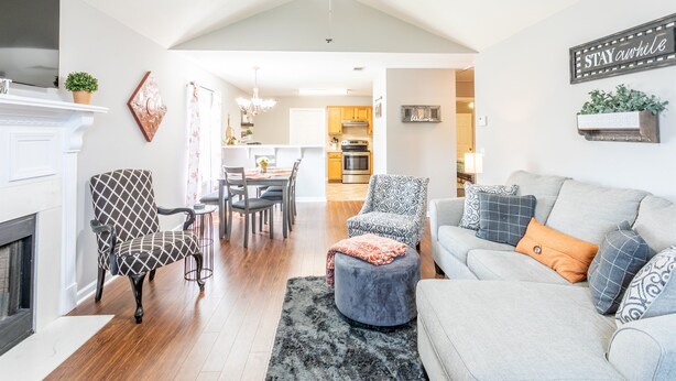 A modern living room with a fireplace, a ceiling fan, a dining area, and a kitchen in the background. - Clean+Cozy+Close to Airport/Jackson/Dogwood Ctr! (Brandon)