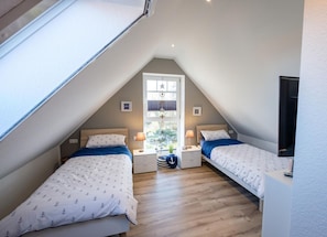 A bedroom with two beds, a sloped ceiling, and a window with blinds.